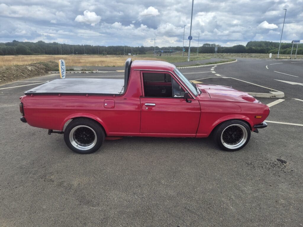 Classic red pickup truck parked on open road under cloudy sky.