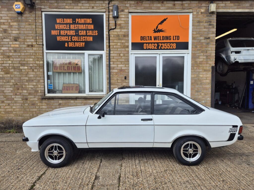 Classic white car parked in front of a brick building with signs.