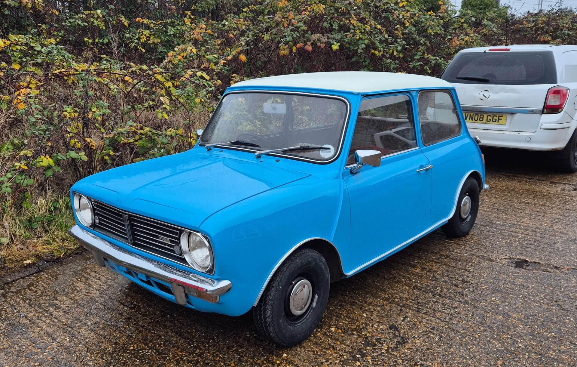 A vintage bright blue car parked outdoors near trees.