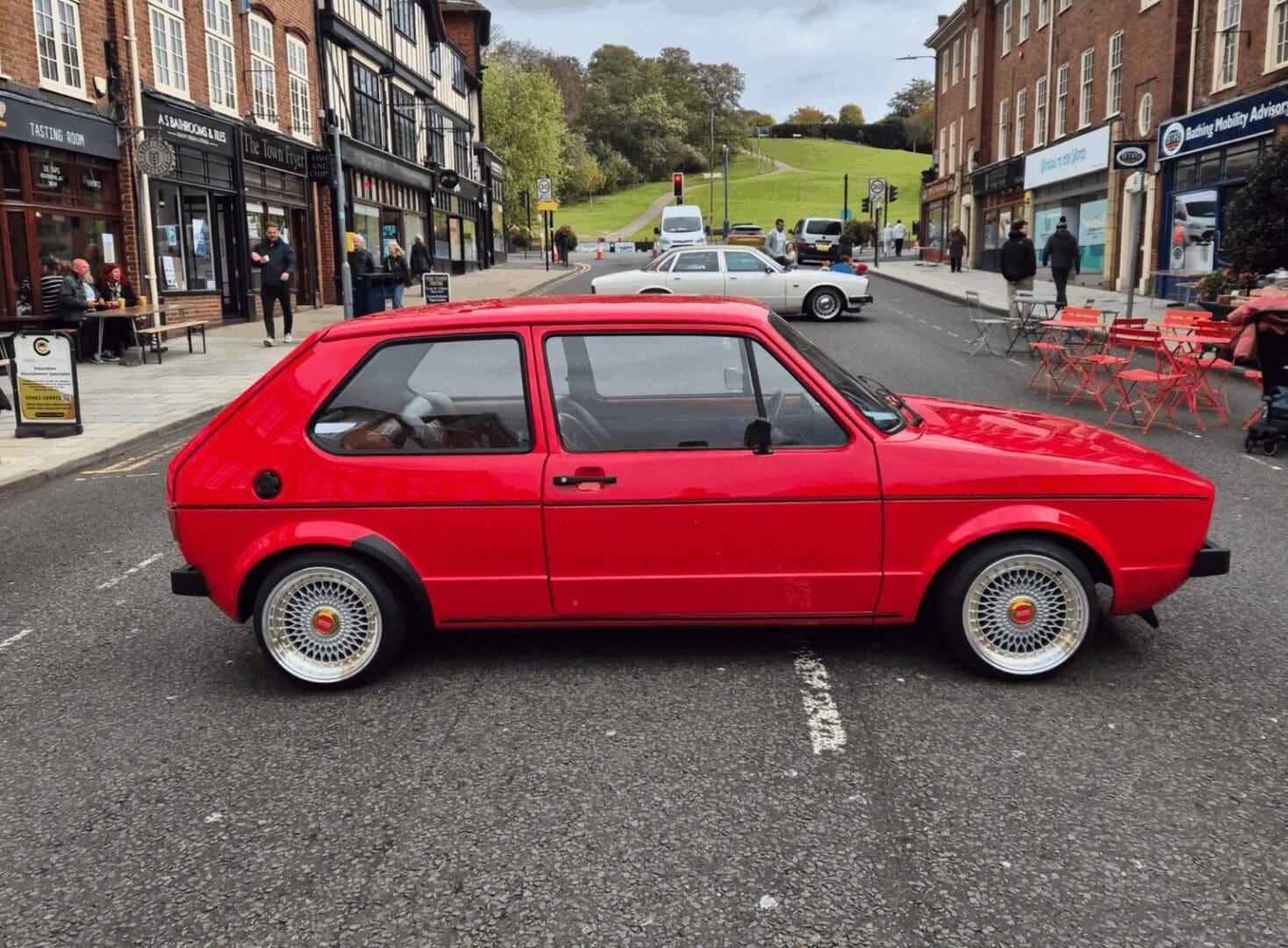A classic red hatchback parked on a street in a quaint town.